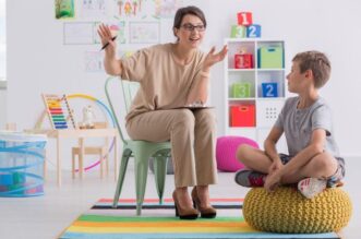 A person sitting on a chair and talking to a child Description automatically generated